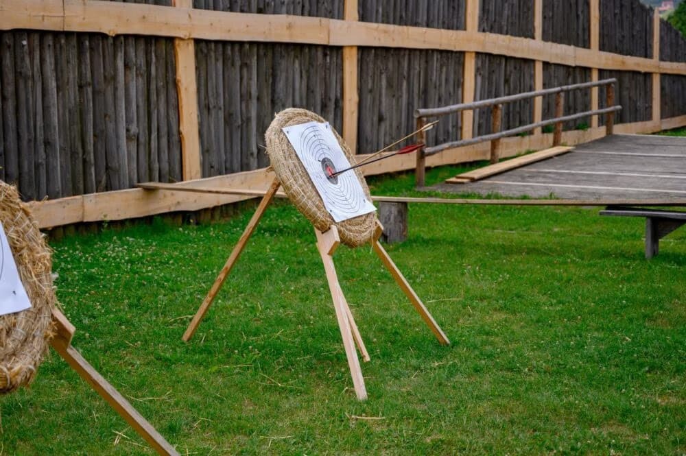 Straw archery targets with arrows in the center stand on a grassy field.